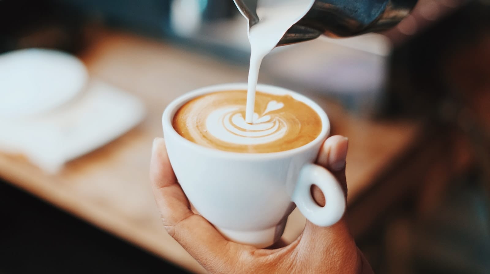 A barista pouring milk into a coffee cup