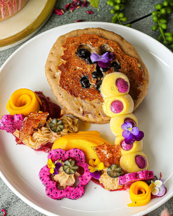 Fluffy vegan pancakes plated with mango roses, dragonfruit and edible flowers