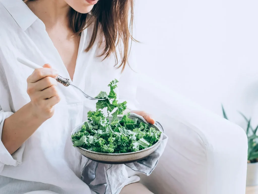 A pregnant woman eating a bowl of fresh leafy greens