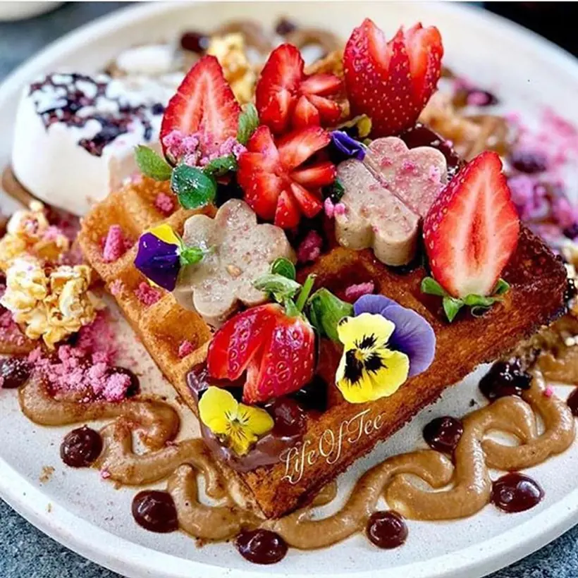 A vegan waffle stack topped with strawberries, edible flowers and nut butter