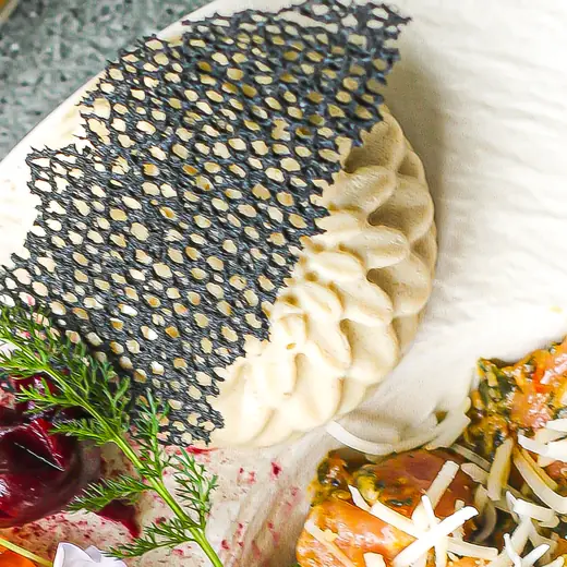 A close-up of a plated curry with a savoury tuile, dumpling and micro herbs