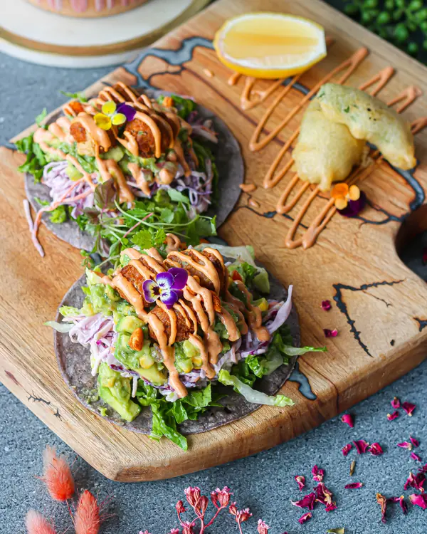 Two vegan tacos on blue corn tortillas with slaw, avocado and chipotle sauce