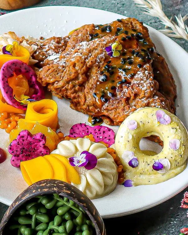 A plated vegan dessert with mango roses, dragonfruit flowers and a doughnut